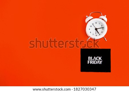 white alarm clock and an inscription on a black square - black Friday on a red background. The topic of sales.