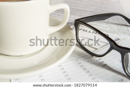 Close-up of black men's elegant glasses and a white coffee Cup standing on business papers.