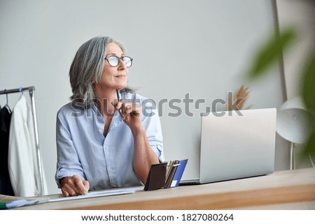 Inspired mature grey-haired woman fashion designer thinking on new creative ideas at workplace. Smiling beautiful elegant classy middle aged older lady small business owner dreaming in atelier studio.