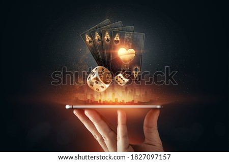 Creative background, online casino, in a man's hand a smartphone with playing cards, roulette and chips, black-gold background. Internet gambling concept. Copy space. Royalty-Free Stock Photo #1827097157
