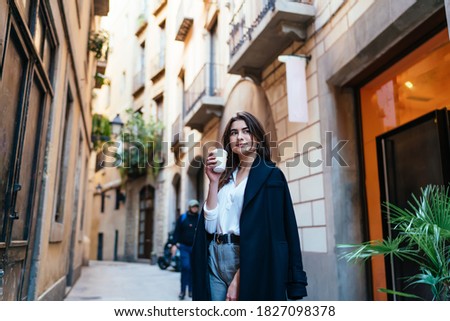 Pensive female tourist in trendy coat standing at street in historic center and pondering on old times, Caucasian hipster girl with disposable takeaway cup thinking during travel sightseeing