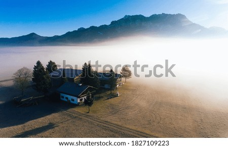 Picturesque drone view of green valley with small village surrounded by trees located near mountain range of Alps in foggy morning