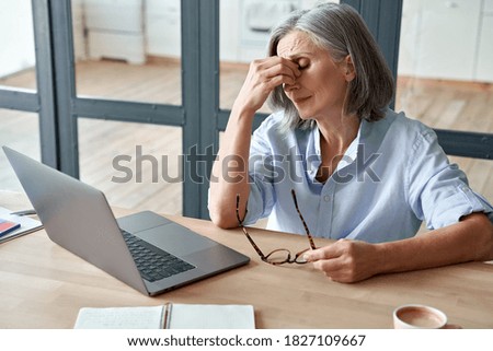 Overworked tired older lady holding glasses feeling headache, having eyesight problem after computer work. Stressed mature senior business woman suffering from fatigue rubbing dry eyes at workplace. Royalty-Free Stock Photo #1827109667
