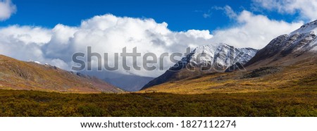 Beautiful Panoramic View of Scenic Valley surrounded by Snowy Mountains in Canadian Nature. Season change from Fall to Winter. Taken near Grizzly Lake in Tombstone Territorial Park, Yukon, Canada. Royalty-Free Stock Photo #1827112274