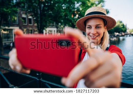 Smiling female in straw hat standing near calm water during photoset while relaxing on street near old house in Amsterdam