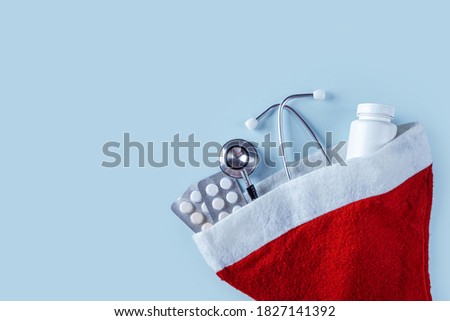 Medical Christmas composition with pills, jar of vitamins and stethoscope in Santa Claus red hat on blue background. Health care and medicne concept for card, calendar, cover. Copy space for text