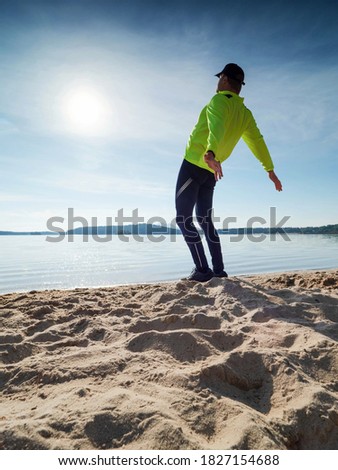 Tall slim man doing stretching on the beach on a sunny morning.  Body stretching before doing sports.
