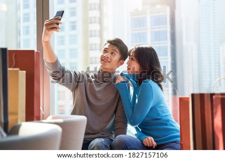 happy young asian couple taking a selfie in hotel room after shopping in the city
