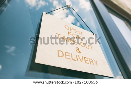 The wooden sign with text: Open for take-out and delivery hanging on the door in cafe