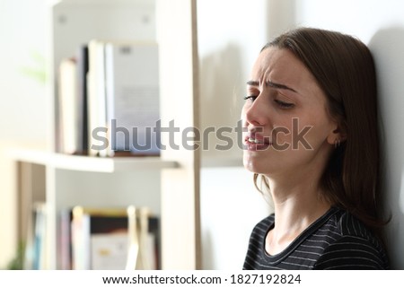 Depressed woman crying alone leaning on a wall at home Royalty-Free Stock Photo #1827192824