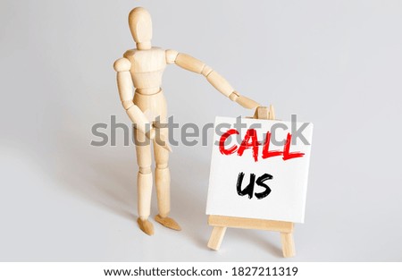 Wooden man shows with a hand to white easel with text CALL US on the white background