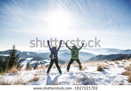 Rear view of senior couple hikers in snow-covered winter nature, jumping.