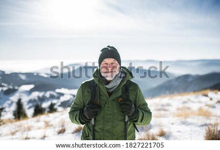 Portrait of senior man standing in snow-covered winter nature, looking at camera.