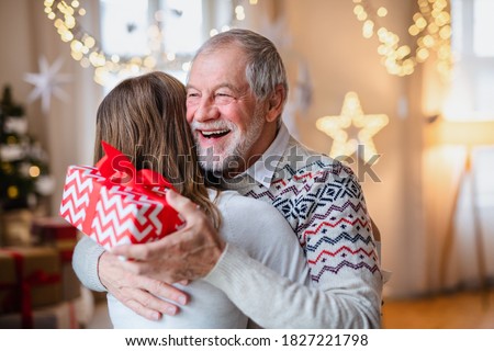 Young woman giving present to happy grandfather indoors at home at Christmas.