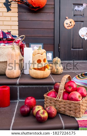 Group of ripe halloween pumpkins, heap of apples in basket, red candle, pictures in frames on porch and other stuff by door of country house