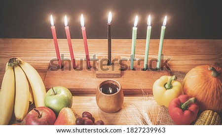 Kwanzaa holiday concept with decorate seven candles red, black and green, gift box, pumpkin,corn and fruit on wooden desk and black background.