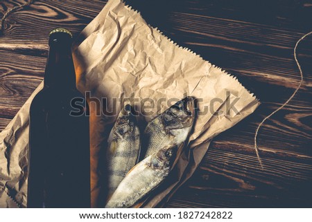 A bottle of beer and dried fish on a paper bag on a wooden table. Studio photo.