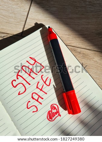 A notebook with an English inscription "Stay safe" and a painted heart. A red permanent marker and retro wooden floor.