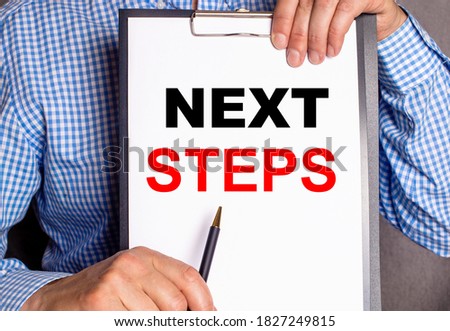 The man points with a pen to the inscription on the sheet of paper NEXT STEPS