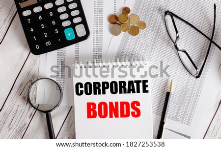 CORPORATE BONDS written in a white notepad near a calculator, cash, glasses, a magnifying glass and a pen. Business concept