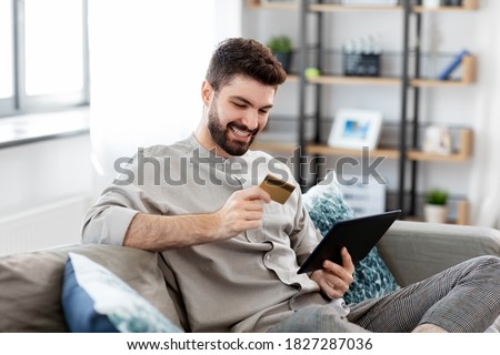 technology, people and online shopping concept - happy smiling man with tablet pc computer and credit card at home Royalty-Free Stock Photo #1827287036