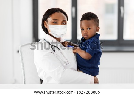 medicine, healthcare, pediatry and people concept - african american female doctor or pediatrician wearing protective mask holding baby boy patient on medical exam at clinic Royalty-Free Stock Photo #1827288806