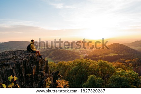 Confident man sitting on the edge. Amazing view  in hilly landscape far from people. Tourist student is relaxing in nature during sunset. Traveling sitting in mountains. Adventure, Art, Travel and Hike concept. Royalty-Free Stock Photo #1827320267