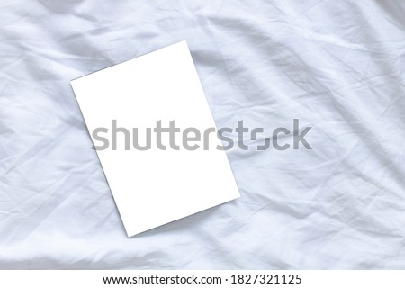 Blank flyer poster mockup on white sheet bed background with copyspace. Top view, flat lay