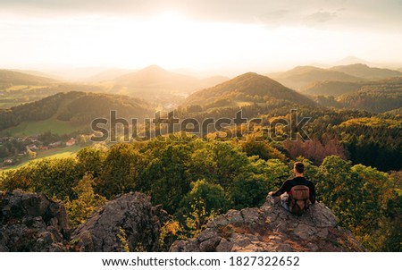 Man traveler sitting on rocky enjoying beautiful mountain view.  Mountain meadow in spring or autumn. Vivid and strong vignetting effect.