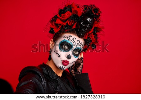 Closeup photo of funny folklore witch, creepy lady calavera with makeup masquerade. Sugar skull girl take selfies wear floral headwear and leather jacket isolated on red background.