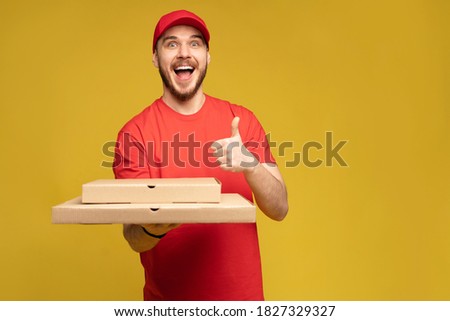 Happy man from delivery service in red t-shirt and cap giving food order and holding pizza box isolated over yellow