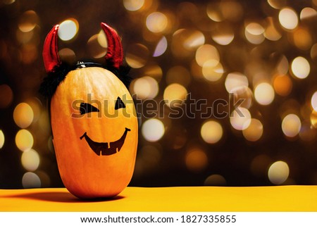 Scary pumpkin with spooky smiling face with devil horns on double orange and black background with lights in shape of scary eyes and faces creating holiday mood with copy space. Halloween concept.