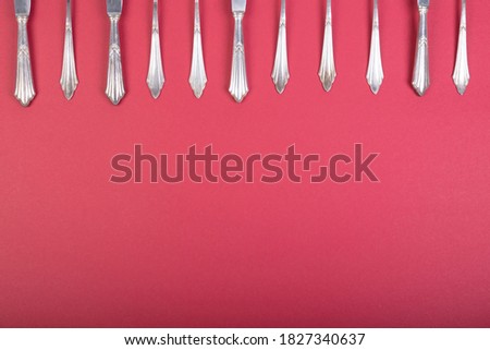 silver cutlery on a white tablecloth, forks, knives and spoons building a frame above, red background