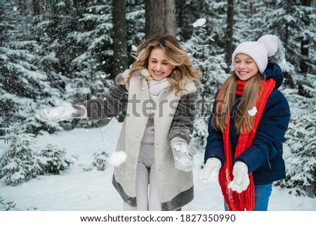 Beautiful young blonde with her charming daughter enjoy the snow outside the city in the forest.