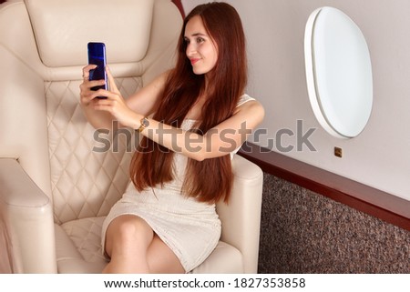 A woman takes a selfie inside the plane. A beautiful female takes pictures of herself on board a private jet.