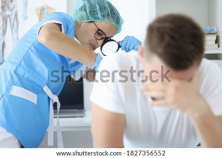 Practitioner doctor with magnifying glass in his hand examines rectum of man patient portrait. Protata cancer prevention annual medical check-ups concept. Royalty-Free Stock Photo #1827356552