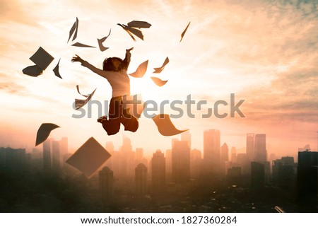 Silhouette of businesswoman expressing her success by jumping on the sky while throwing papers with dusk sunlight background