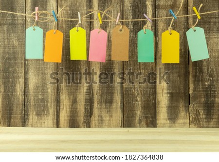Eight price tags in different colors with space for text. Tags and inscriptions for text on a wooden background. The labels are hung on a rope with multi-colored clothespins