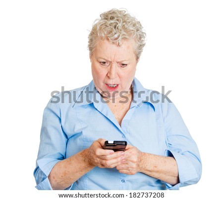 Closeup portrait of upset, sad, senior mature woman shocked by what she sees on her cell phone, an sms, text message or email, isolated white background. Negative emotion facial expression feelings.