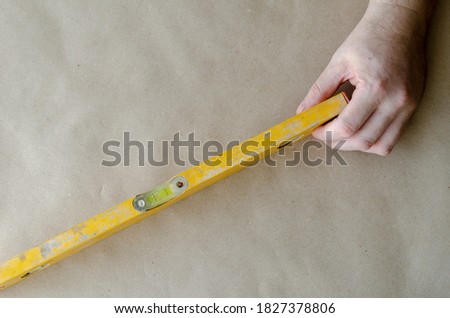 Hand of an adult Caucasian man holds a yellow construction level. A real hand tool with scratches and traces of cement. The construction industry. Selective trick.