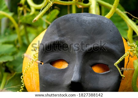 Fragment of a ceramic black mask with empty eyes on a background of orange pumpkin. Scary Halloween. Mass production mask.