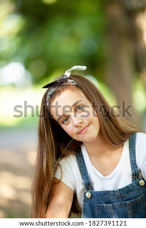 beautiful girl teenager in denim overalls with a blade of grass in her teeth