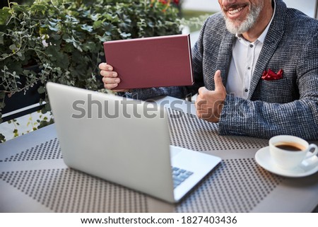 Cropped copy-space photo of a bearded man showing thumbs up and holding a dar-red box near a laptop