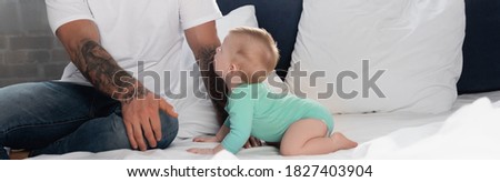 panoramic concept of infant boy in baby romper crawling on bed near father