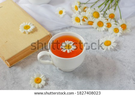 a Cup of tea with chamomile and a bouquet of daisies in a vase