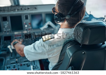 Top view of man in aviation uniform and earphones sitting at control and switching rudder while taking off Royalty-Free Stock Photo #1827461363