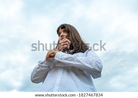 Low angle portrait of a pretty brunette woman in a white shirt, outdoors, against the sky