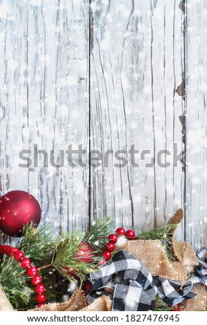 Snowy Christmas background with holiday trimmings of pine tree branches, ornaments, black and white buffalo check ribbon, burlap and red bead garland.. Top view with copy space available.