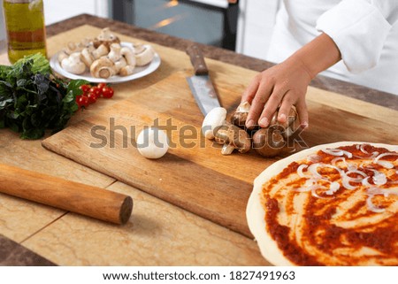 View of the hands of a chef preparing mushrooms for chopping on a wooden board.