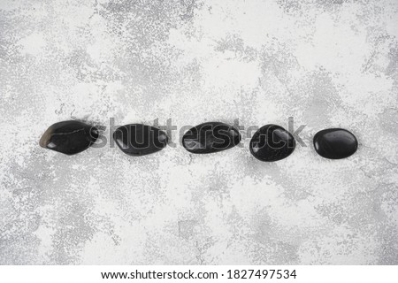 Black spa stones line on gray concrete background. Wellness concept. Top view, flat lay, copy space